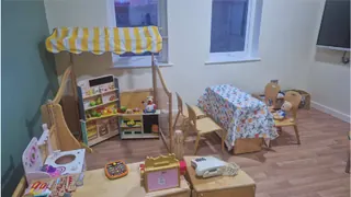 A role-play room with a toy market stall, a play kitchen and a table set for tea