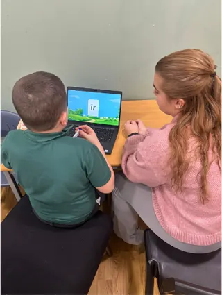 A pupil working on a laptop with support from a member of staff
