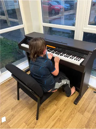 A pupil playing a digital piano beside a large window