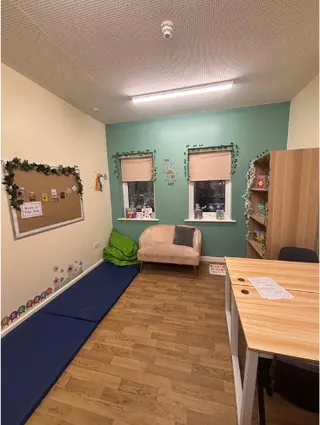 A calm room with soft seating, floor mats, bookshelves and a desk