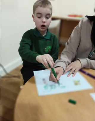 A pupil in school uniform drawing with support from a member of staff